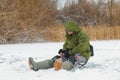 A fisherman is fishing in an ice hole on a frozen pond.