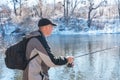 A fisherman with a fishing rod and a backpack catches fish on the bank of a snow-covered river in early spring Royalty Free Stock Photo