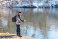 A fisherman with a fishing rod and a backpack catches fish on the bank of a snow-covered river in early spring Royalty Free Stock Photo