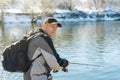 A fisherman with a fishing rod and a backpack catches fish on the bank of a snow-covered river in early spring Royalty Free Stock Photo