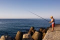 Fisherman with fishing rod standing on the pier, view on the horizon