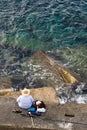 Fisherman is fishing on sea stone, top vertical