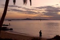 Fisherman fishing on a tropical beach. Coconut palm tree silhouette. Sea pink sunset.