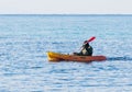 Fisherman in green jumpsuit floats in orange kayak on sea