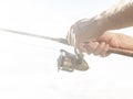 Fisherman hands close up holding spinning reel rod or spoon bait over white overexposed foggy dreamy background