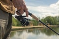 Fisherman hands holding and rotating spinning reel rod and fishing over river, close up Royalty Free Stock Photo