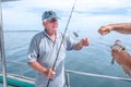 Fisherman helping caucasian tourist on fishing charter boat taking hook out of snapper fish - at Doubtless Bay, Far Royalty Free Stock Photo