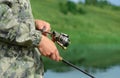 Fisherman is holding a fishing rod in his hands and reeling line on the spool, close-up. Rotation of the reel is creating a