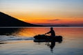 Fisherman in an inflatable boat floats on the lake. Silhouette on a sunset background Royalty Free Stock Photo