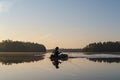 Fisherman in an inflatable boat rowing on a calm forest lake, at dawn, against a background of sky and trees. Beautiful Royalty Free Stock Photo