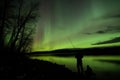 fisherman at lake under a night sky aglow with aurora from a geomagnetic storm