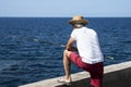 Fisherman on the oceanfront. A man in a white shirt and straw hat catches fish. Madeira. Portugal. Europe.