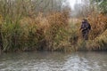 A fisherman in professional gear stands on the bank of a river with a fishing rod in his Royalty Free Stock Photo