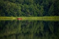 A fisherman in a red boat is fishing in the lake. Beautiful summer landscape with a forest lake. Royalty Free Stock Photo