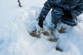 Fisherman removes ice from a drilled hole with a scoop, a drill stands nearby. Preparing for winter fishing. Hobbies and