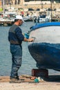 Fisherman repairing and painting an old wooden fishing boat at the port quay