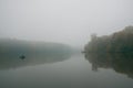 Fisherman in a rubber boat fishing with rods on a small lake, deep fog on a cold autumn morning Royalty Free Stock Photo