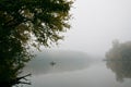 Fisherman in a rubber boat fishing with rods on a small lake, still water surface, reflection and deep fog on an autumn morning Royalty Free Stock Photo