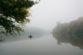 Fisherman in a rubber boat fishing with rods on a small lake, still water surface, reflection, deep fog on a cold autumn morning Royalty Free Stock Photo