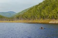 A fisherman on a rubber boat with oars floats on a calm lake amid green hills Royalty Free Stock Photo