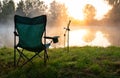 Fisherman's chair and fishing rods in the background over the lake at sunrise, foggy morning. Fishing concept. Royalty Free Stock Photo