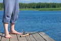 fishermans feet on the pier, near the fishing rod lies on the background of the lake