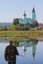 Fisherman`s figure with a fishing rod on a bank of river Riv with Trinity convent of russian orthodox church, mirror reflections