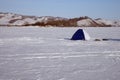 Fisherman`s tent is on the snow-covered ice of the lake, against the backdrop of the shore.
