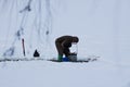 Fisherman silhouette collecting bloodworm by washing it out from bottom mud with a metal sieve in ice hole