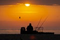 Fisherman silhouette fishing in the Sea or Ocean beach during sunrise. Swinging a rod