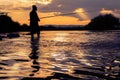 Fisherman silhouette standing in the water with his rod at suns