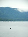 A fisherman sits in a boat in the middle of a large lake surrounded by mountains in the rain Royalty Free Stock Photo