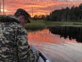 A fisherman sits in a boat during sunset on the lake, calm