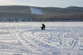 The fisherman sits and catches fish on the snowy lake, in the evening.