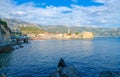 Fisherman sits on rocks against background Old Town of Budva, Montenegro