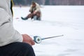 The fisherman sits with winter fishing rod in hand in the foreground, in the background blurred silhouettes of the fishermen on ic