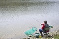 Fisherman Sitting In The Chair On The Riverside Reeling String And Throwing Rod Into The River