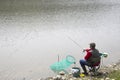 Fisherman Sitting In The Chair On The Riverside Reeling String And Throwing Rod Into The River