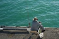 Fisherman sitting on the pier at the blue calm sea