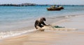 Fisherman sitting on a white sand beach shore in the morning sun fixing his net. Royalty Free Stock Photo