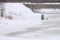 A fisherman speaks on the phone on a frozen river under a bridge Royalty Free Stock Photo