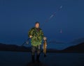 Fisherman standing on lake shore and holding spinning rod and big salmon fish caught at night Royalty Free Stock Photo
