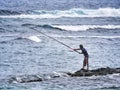 Fisherman standing on rocks defying waves with fishing rod