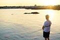 Fisherman standing at the seashore hooks a fish against sunset. Sportsman holds a fishing rod and reel in a hooked fish. Spin