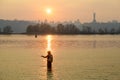 Fisherman stands in the river Dnipro. Sunset over Kyiv and the Motherland Monument. Ukraine.