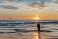 Fisherman stands on sandy beach during sunset