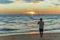 Fisherman stands on sandy beach during sunset