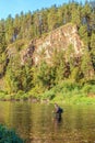 A fisherman stands in the water and fishes in a mountain river.