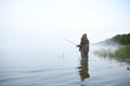 Fisherman stands in the water on the lake in fog