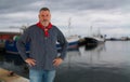 A fisherman with a typical shirt stands at the harbor. In the background are fishing boats. Royalty Free Stock Photo